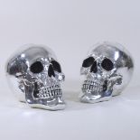 A pair of silver painted models of skulls,