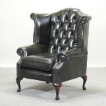 A green leather upholstered button back wing armchair, on cabriole legs,
