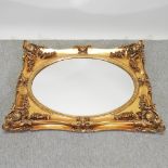 An ornate gilt framed wall mirror, with an inset oval plate,