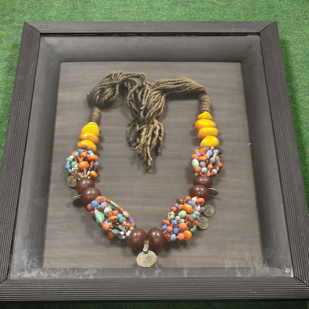 A North African copal amber and coloured bead necklace, in a glazed display frame,