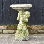 A reconstituted stone bird bath in the form of a cherub,