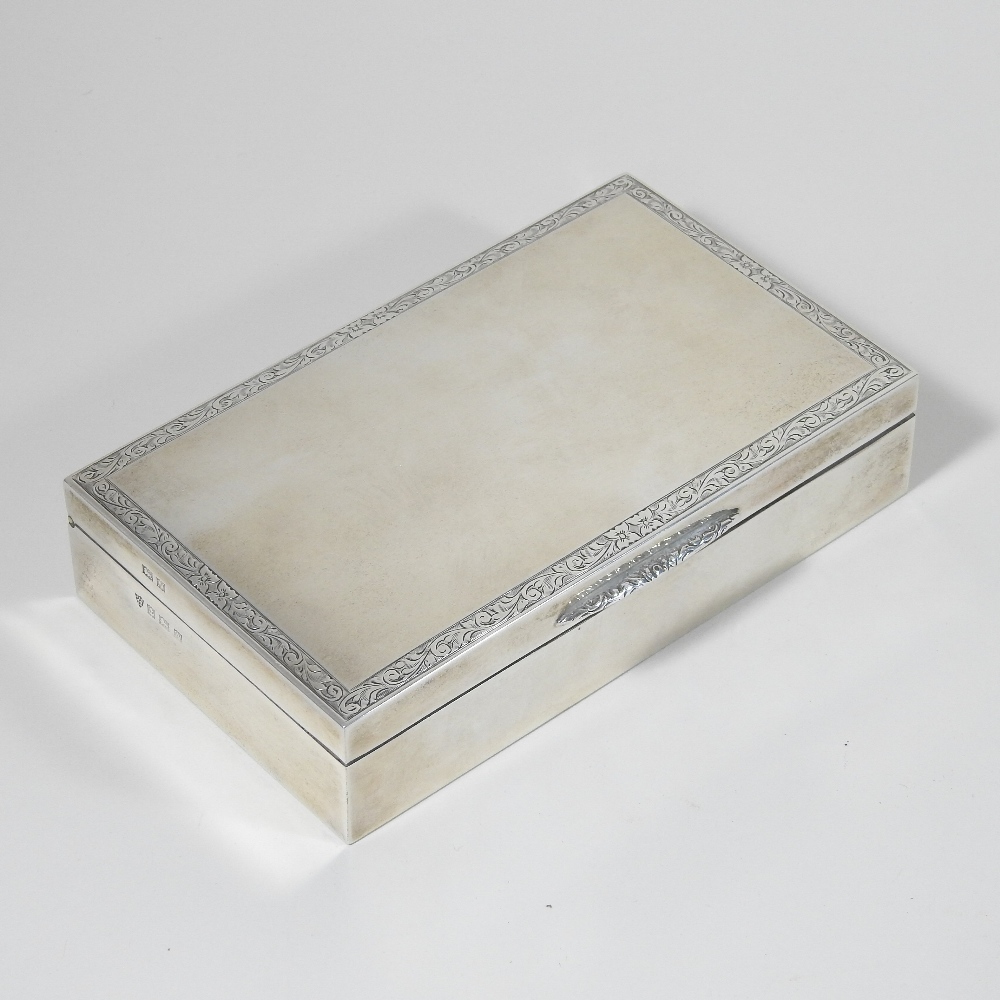 A modern silver table cigarette box, of hinged rectangular shape, with an engraved scrolled border,