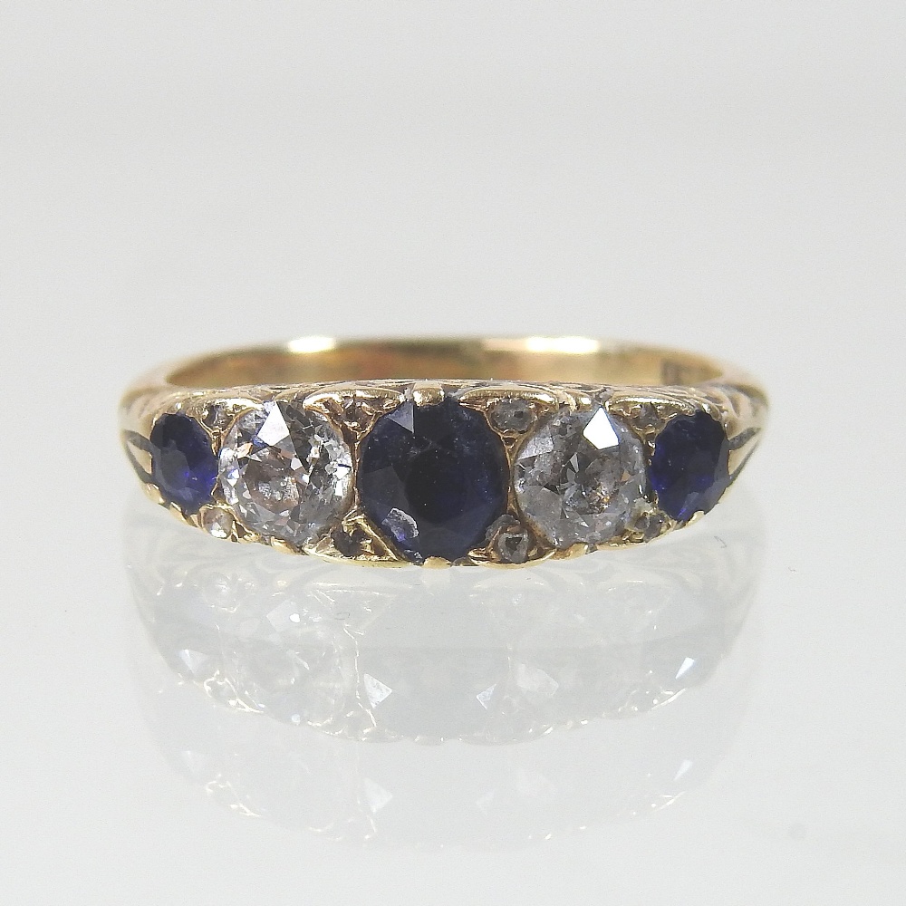 An early 20th century 18 carat gold sapphire and diamond five stone ring, with textured shoulders,