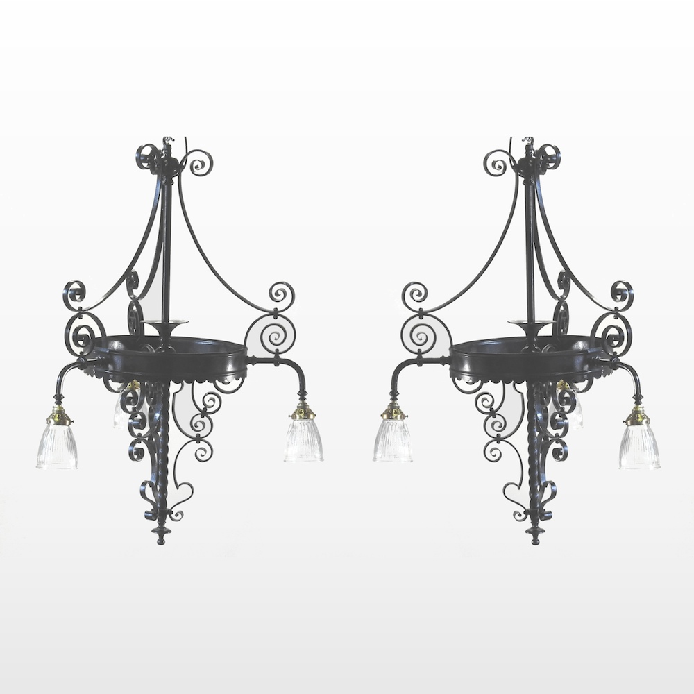 A pair of antique black painted wrought iron three branch chandeliers, with glass shades,