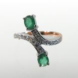 A modern 14 carat gold, emerald and diamond ring, of crossover design,