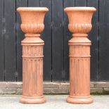 A pair of terracotta garden planters, each on a fluted stand,