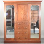 An Edwardian mahogany and inlaid combination triple wardrobe, enclosed by mirrored doors,