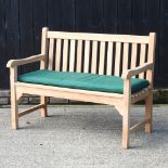 A teak slatted garden bench, with a loose cushion,