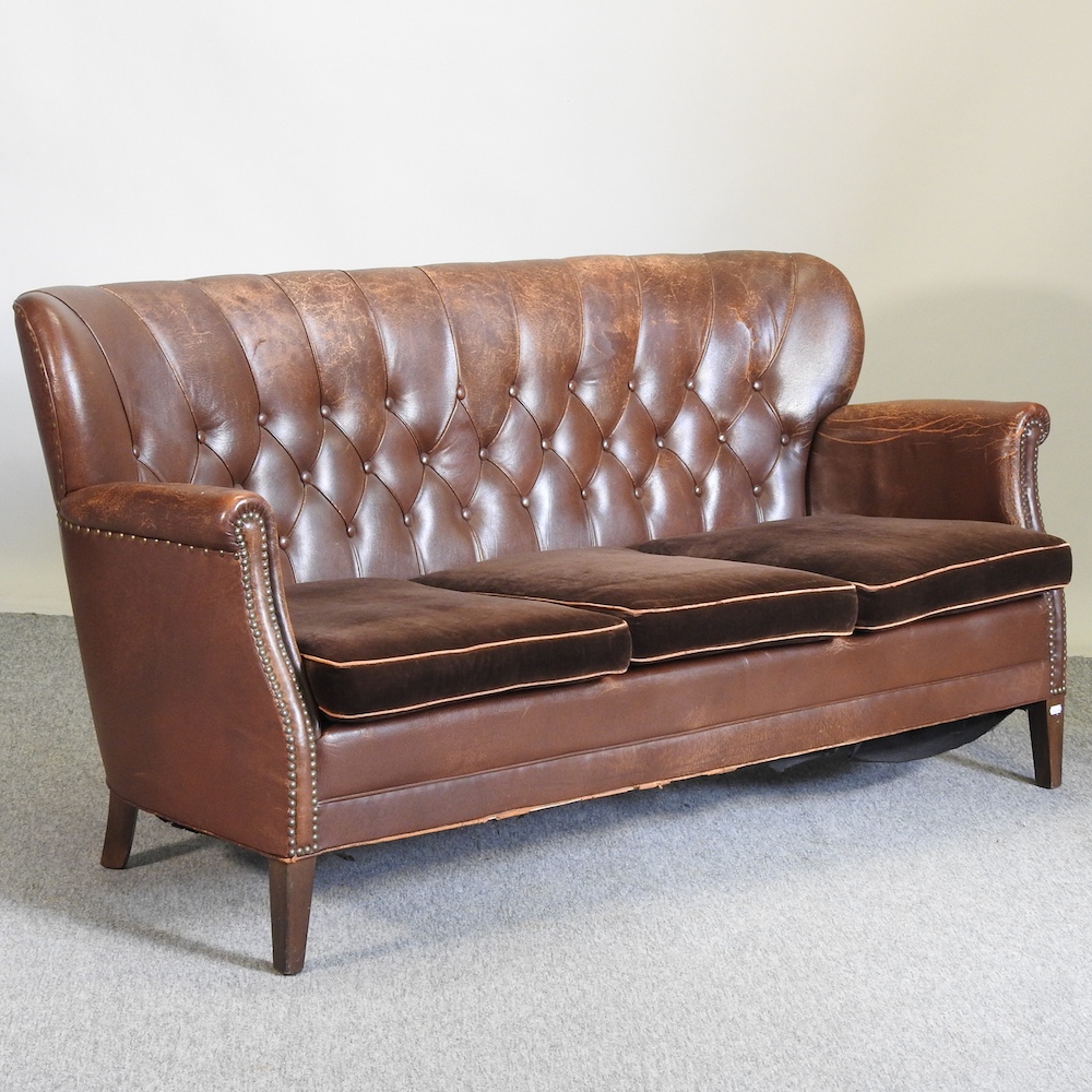 A 1920's brown leather upholstered sofa, with velvet cushions,