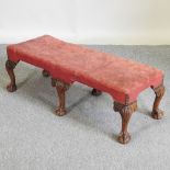 A red upholstered footstool, on six legs, with claw and ball feet,
