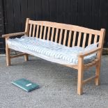 A teak slatted garden bench, with a loose cushion and cover,