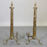 A pair of large brass fire dogs, each in the form of a column, surmounted by an urn,