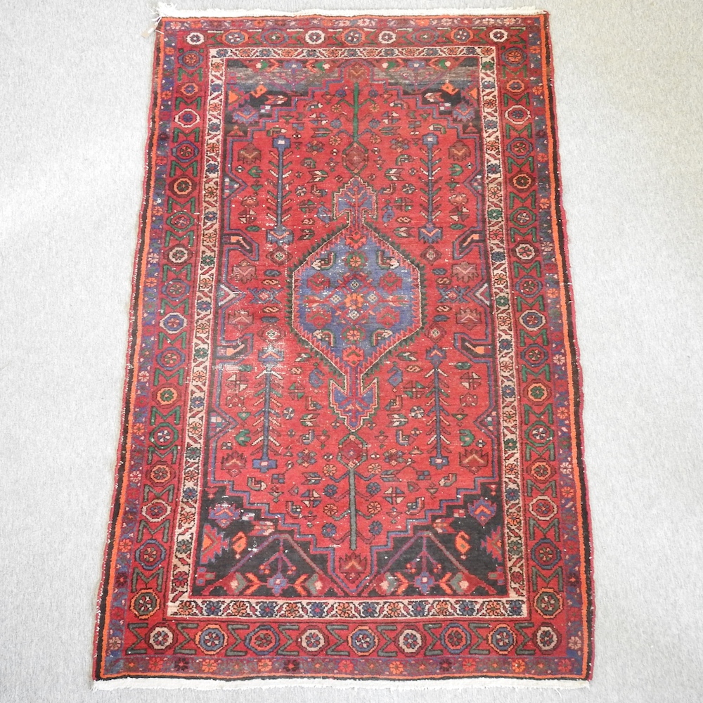 A Persian woollen rug, with geometric design, on a red ground,