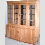 An antique pine breakfront bookcase, enclosed by glazed doors, with cupboards below,