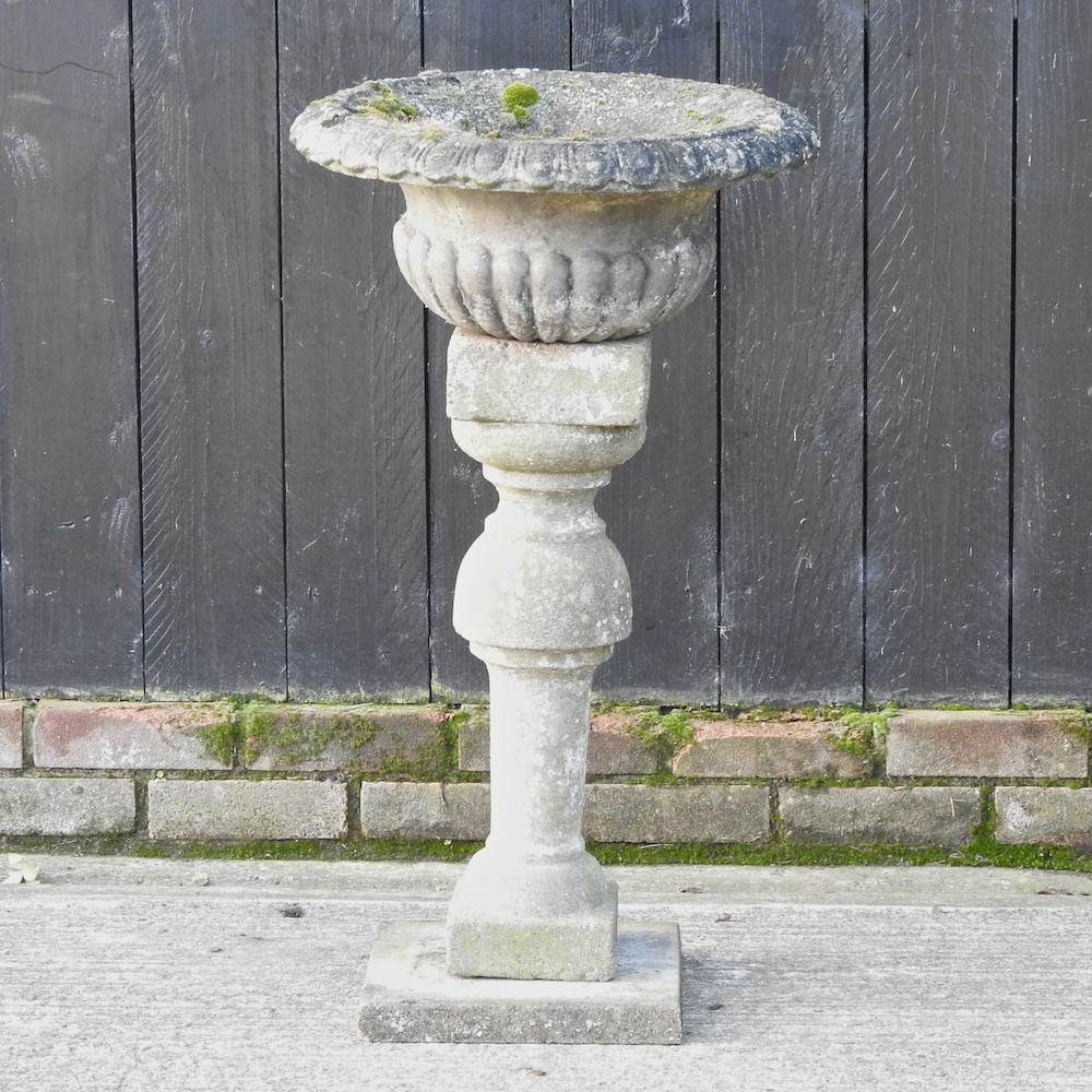 A reconstituted stone urn, on a column base,