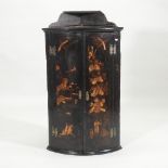 A George III black japanned bow front hanging corner cupboard, with painted relief decoration,