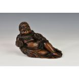 A Chinese carved boxwood figure of a reclining Buddha, 18th / 19th century, the smiling figure