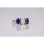 An 18ct white gold, diamond and sapphire trilogy ring, the central oval cut diamond weighing