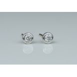 A pair of white gold and diamond stud earrings, each diamond in a bezel setting and weighing