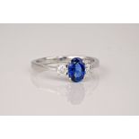 A white gold, sapphire and diamond three stone ring, the central oval cut sapphire of a deep,