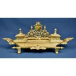 An ornate brass desk stand the double inkwell stand in a Neoclassical Style, 16in. (40.7cm.) long.