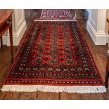 A Bokhara rug, late 20th century, with three rows of eleven gols on a madder field, within a