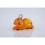 A Chinese amber pendant in the shape of a dog, with visible inclusions and measuring 27x15mm.