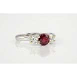 An 18ct white gold, ruby and diamond three stone ring, the central, round cut ruby weighing