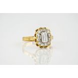 An 18ct yellow gold and diamond cluster ring, the central, emerald cut diamond measuring