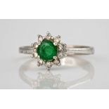 An 18ct white gold, emerald and diamond cluster ring, the central round cut emerald weighing