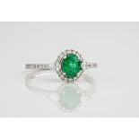 An 18ct white gold, diamond and emerald ring., With the central oval cut emerald surrounded by a