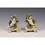 A pair of late 18th century Chelsea porcelain figures of cupid, crouched alongside a flowering tree,
