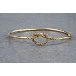 A 9ct gold hinged bangle with diamond set knot detailing, approximately 63mm in diameter.