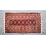 An Afghan rug, the row of seven octagonal gols on a madder field, within a rosette border and