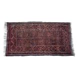 A Beluch rug, the faded madder field with a central panel of pairs of indigo and brown gols,