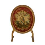 A George III oval giltwood firescreen, the curled ribbon decorated frame enclosing a tapestry