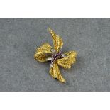 An 18ct gold, ruby and diamond floral bow brooch, formed of textured gold ribbon with floral ruby