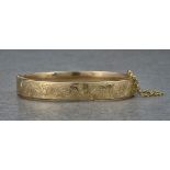 A 9ct hollow yellow gold hinged bangle, with foliate and scrolled engraving details to the top half.