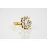 An 18ct yellow gold and diamond cluster ring, the central, emerald cut diamond measuring approx. 0.