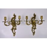 Twelve twin branch brass wall lights, with ornate shaped and pierced flaming sconce backplates,