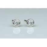 A pair of white gold and diamond stud earrings, each diamond in a bezel setting and weighing