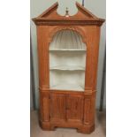 A full height stripped pine corner cupboard in the Georgian style, with arched pediment, open