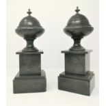 A pair of polished black slate mantel urns on square bases, brass finials, 31 cm