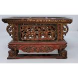 A Chinese wooden tea pot stand in red and gilt with carved and pierced decoration of figures and