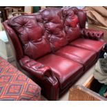 A 3 seater settee in the traditional deeply buttoned wing back style red leather