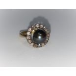 A lady's dress ring set with central black pearl surrounded by an outer ring of 16 small diamond