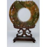 A Chinese carved jade colour stylized circular stone with incised decoration, on hardwood stand (