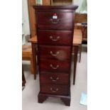 A tall narrow chest of drawers in dark wood;