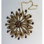 A yellow metal circular sunburst brooch set 2 concentric rows of garnets, and central domed