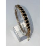 An Edwardian 9 carat hallmarked gold hinged filigree bangle, set 9 oval graduating sapphires, 15.4